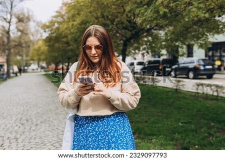Outdoor lifestyle fashion portrait of woman posing on the street. Close up of woman holding eco or reusable shopping bag and using smartphone outdoors. Urban lifestyle concept