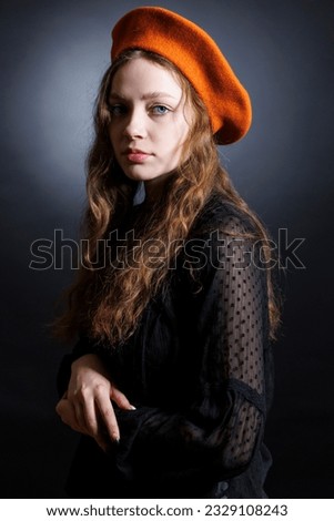 Portrait of a sad young woman in an orange beret and long curly hair on a dark background.