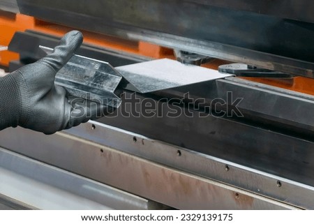 Close up the bending machine operator hold the sheet metal parts and  wear safety  rubber glove. The sheet metal working operation by skill operator. Royalty-Free Stock Photo #2329139175