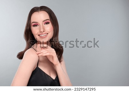 Portrait of beautiful young woman with makeup and gorgeous hair styling on light grey background. Space for text