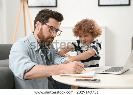 Little boy bothering his father at home. Man working remotely at desk Royalty-Free Stock Photo #2329149751