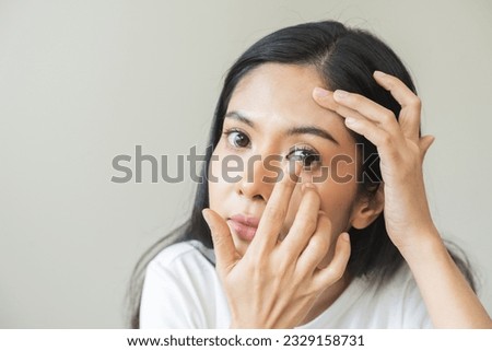 Ophthalmology care, eye sight or vision. Closeup asian young woman, female hand holding and putting, wearing soft contact lenses on face with finger, look into eye on background. Medicine and health. Royalty-Free Stock Photo #2329158731