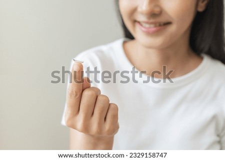 Ophthalmology care, eye sight, vision concept. Closeup happy smile asian young woman, female hand holding, putting, wearing soft contact lenses with finger in front of her face, isolated on background Royalty-Free Stock Photo #2329158747