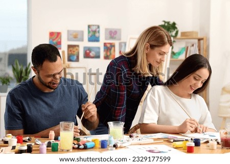 Artist teaching her students to paint at table in studio. Creative hobby