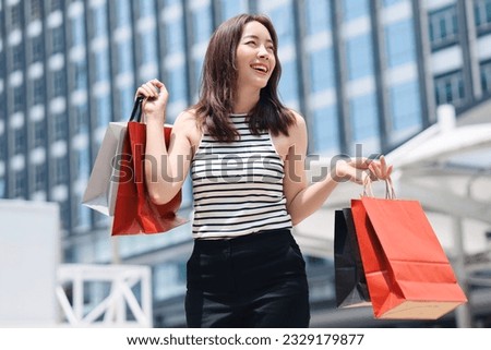 Cheerful Asian woman holding shopping bags.Beautiful Asian woman in casual style shopping in the city. Royalty-Free Stock Photo #2329179877