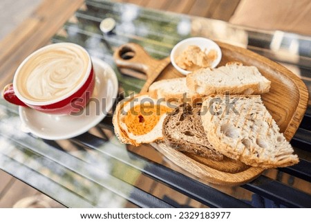 Assorted sliced bread on a wooden board. Served with smoked butter. Breakfast with cappuccino coffee. Composition with butter and bread on wooden plate.