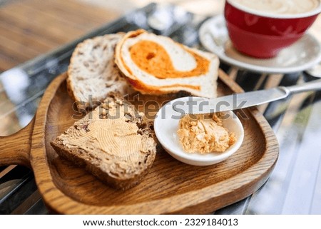 A slice of bread with butter on a chopping board. Assorted sliced bread on a wooden board. Served with smoked butter. Breakfast with cappuccino coffee. 
