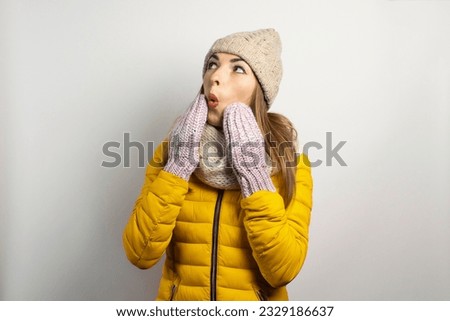 Young woman in a hat and mittens caps on a light background. Winter concept, winter fashion, winter clothes. Funny mood, emotions, surprise, shock.