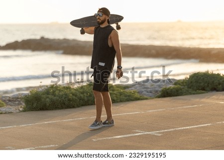 A man walking on the road near by beach holding a skateboard on his shoulder
