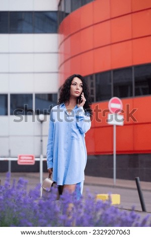Portrait of a beautiful business woman office worker in a long blue shirt with a smartphone on the background of the cityscape
