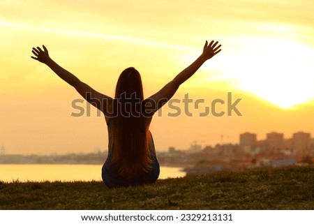 Back view portrait of a silhouette of a woman celebrating at sunset in outskirts