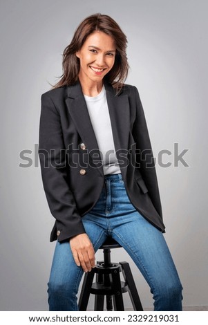 Portait of an attractive businesswoman wearing black blazer and blue jeans against isolated grey background. Copy space.  Royalty-Free Stock Photo #2329219031