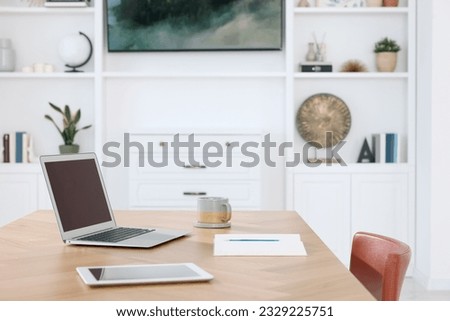 Interior design. Cosy workplace with laptop, tablet and cup on wooden table near tv area. Space for text