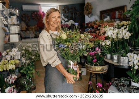 Attractive woman flower shop owner in apron holding bouquet of flowers at florist store Royalty-Free Stock Photo #2329232635