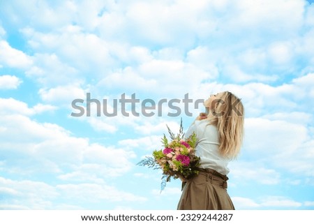 Portrait of young european woman with lush flower bouquet looking up at the blue sky. Dreaming person. Beautiful girl. Natural cloudy background. International woman day. Lifestyle. Copy space. Banner