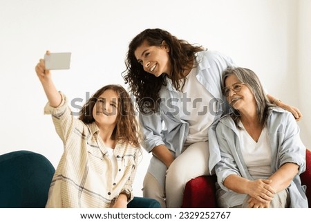 Glad european adult, senior women and teen girl sit on sofa, make selfie on smartphone in living room interior. Family, photo female generation, relationship mom, grandma and daughter, video call