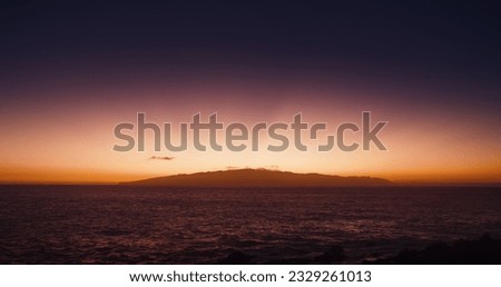 Magical sunset sky and glowing treasure Island La Gomera, Canary, Spain. Silhouette of small island in dark ocean water at dusk. Royalty-Free Stock Photo #2329261013