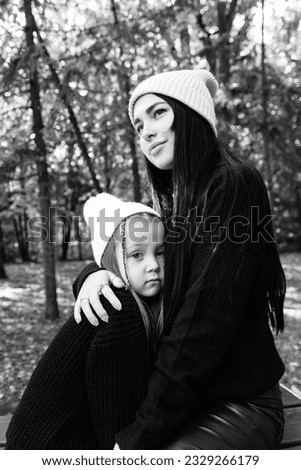 Mom and little daughter. Mom hugs her daughter and hugs her. Tenderness. Summer park. Green trees. The concept of a young family. Black and white photography.