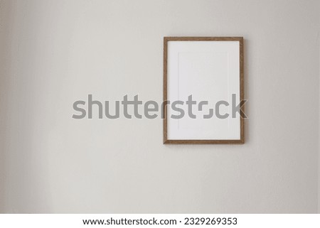 Vertical wooden picture frame mockup hanging on beige wall. Poster mock-upframe on pastel background in sunlight. Home interior with soft shadow, empty copyspace. Art display concept. Minimal interior