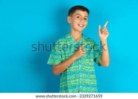 Little hispanic kid boy wearing green aztec shirt smile excited directing fingers look empty space