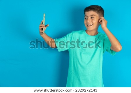 Little hispanic kid boy wearing green T-shirt smiling and taking a selfie ready to post it on her social media.