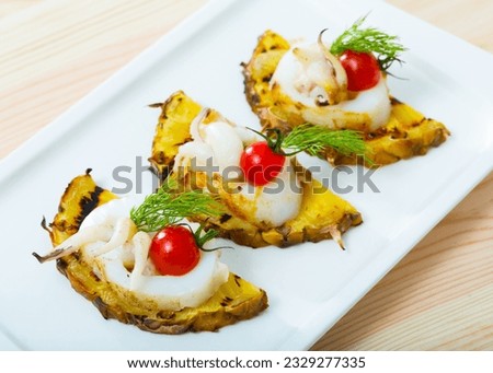 Image of sepia fried on a grill with pineapple, cherry tomatoes and sauce Chile on the plate indoors.