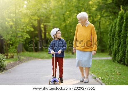 Beautiful granny and her little grandchild walking together in autumn park. Boy riding by scooter. Active family leisure. Royalty-Free Stock Photo #2329279551