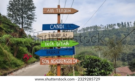 Directional signs for information on places that are in a tourist spot in the hills of a tea garden,shady and green trees, clear and cloudy sky background.no people.