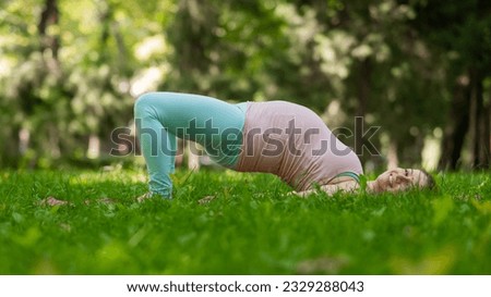 Pregnant caucasian woman doing yoga in the park. Prenatal shoulder bridge exercise. 