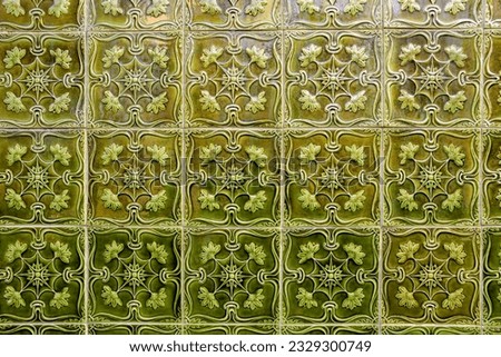 A panel of green tiles with embossed decoration covering a wall
