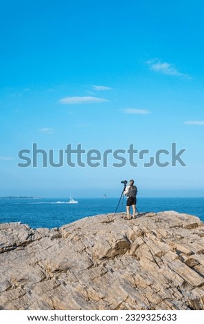 Photographer staying on rocks near ocean and taking photo of selling ship . 