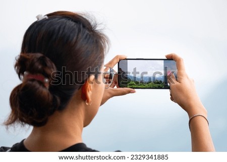 A woman uses her smartphone to take pictures of the sunrise in a valley with abundant nature tourism and technology.