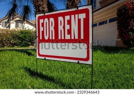A red For Rent sign on a lawn in front of a house 
