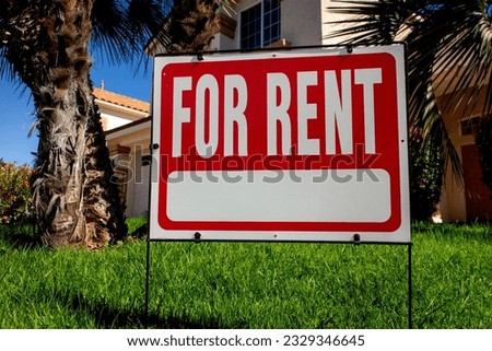 A red For Rent sign on a lawn in front of a house 