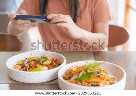 Asia woman eat lunch with feeling happy and enjoy to eat shrimp spaghetti stir fry in restaurant in relax fun with cell phone take a photo of her food for upload to social media. Enjoy food concept.