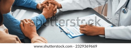 Doctor providing compassionate healthcare consultation while young couple patient holding hand, comfort each other after infertile report. Reproductive and medical fertility consulting. Neoteric Royalty-Free Stock Photo #2329369669