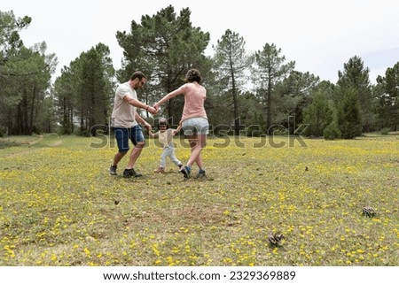 Father, mother and their little daughter playing the Ring Around the Rosy in a meadow full of yellow wildflowers. Royalty-Free Stock Photo #2329369889