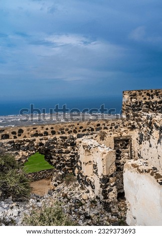 The ruined ancient wall of the fortress in the Pyrgos village in a blur background of the buildings, land, and coastline from afar