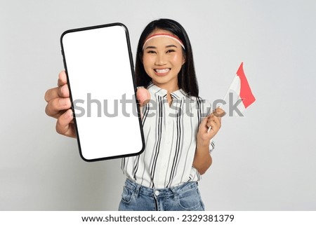 Excited young Asian women celebrate Indonesian independence day while holding smartphone with blank screen and Indonesian flags isolated on white background Royalty-Free Stock Photo #2329381379