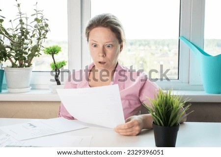 woman surprised by utility bills, Shocked woman looking at letter, reviewing papers with bank documents Royalty-Free Stock Photo #2329396051