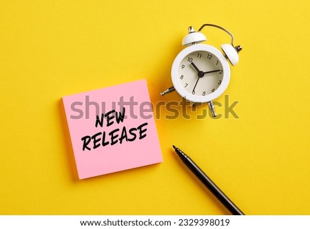 New release message on pink note paper with alarm clock and pen. Marketing concept for new publishing and advertising products.
