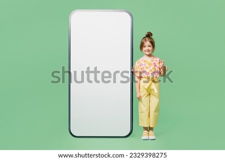 Full body happy fun little child kid girl 6-7 years old wear casual clothes big blank screen area mobile cell phone show thumb up isolated on plain green background. Mother's Day love family concept