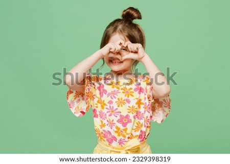 Little cute child kid girl 6-7 years old wear casual clothes look through shape heart with hands heart-shape sign isolated on plain pastel green background Mother's Day love family lifestyle concept Royalty-Free Stock Photo #2329398319