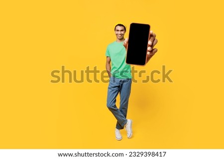Full body young man of African American ethnicity wears casual clothes green t-shirt hat hold use mobile cell phone with blank screen workspace area isolated on plain yellow background studio portrait