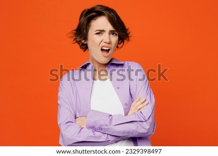 Young irritated indignant annoyed sad caucasian woman she wearing purple shirt white t-shirt casual clothes hold hands crossed isolated on plain orange background studio portrait. Lifestyle concept Royalty-Free Stock Photo #2329398497