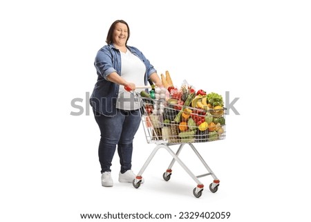 Full length shot of an overweight woman standing with a full shopping cart isolated on white background