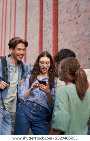 University students browsing phone next to university campus building Royalty-Free Stock Photo #2329405055