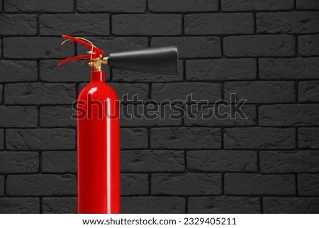Fire extinguisher against grey brick wall, space for text