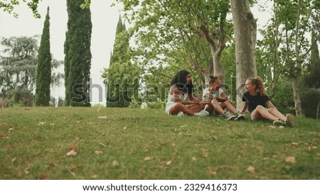 Three girls friends pre-teenage sit on the grass in the park and emotionally talking. Three teenagers on the outdoors Royalty-Free Stock Photo #2329416373