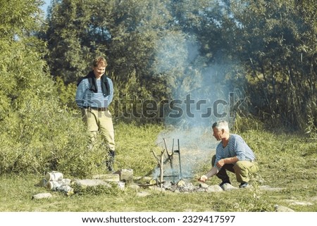 Two men, after successful fishing, fry a barbecue of fish on a fire in field conditions. High quality photo